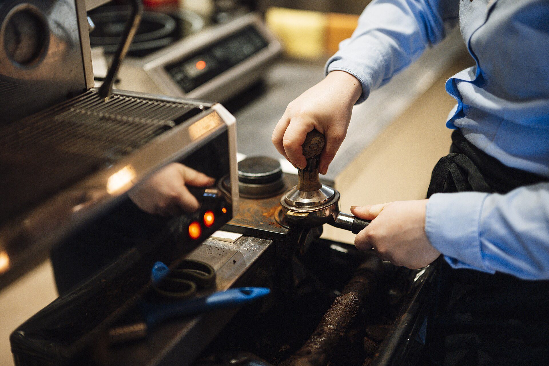 Mani al lavoro sul gruppo e sui comandi di una macchina da caffè professionale